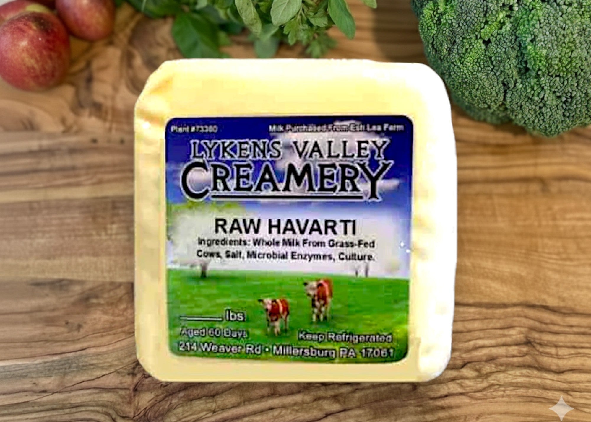 Block of Lyken's Valley Creamery Raw Havarti cheese on a wooden surface with vegetables in the background