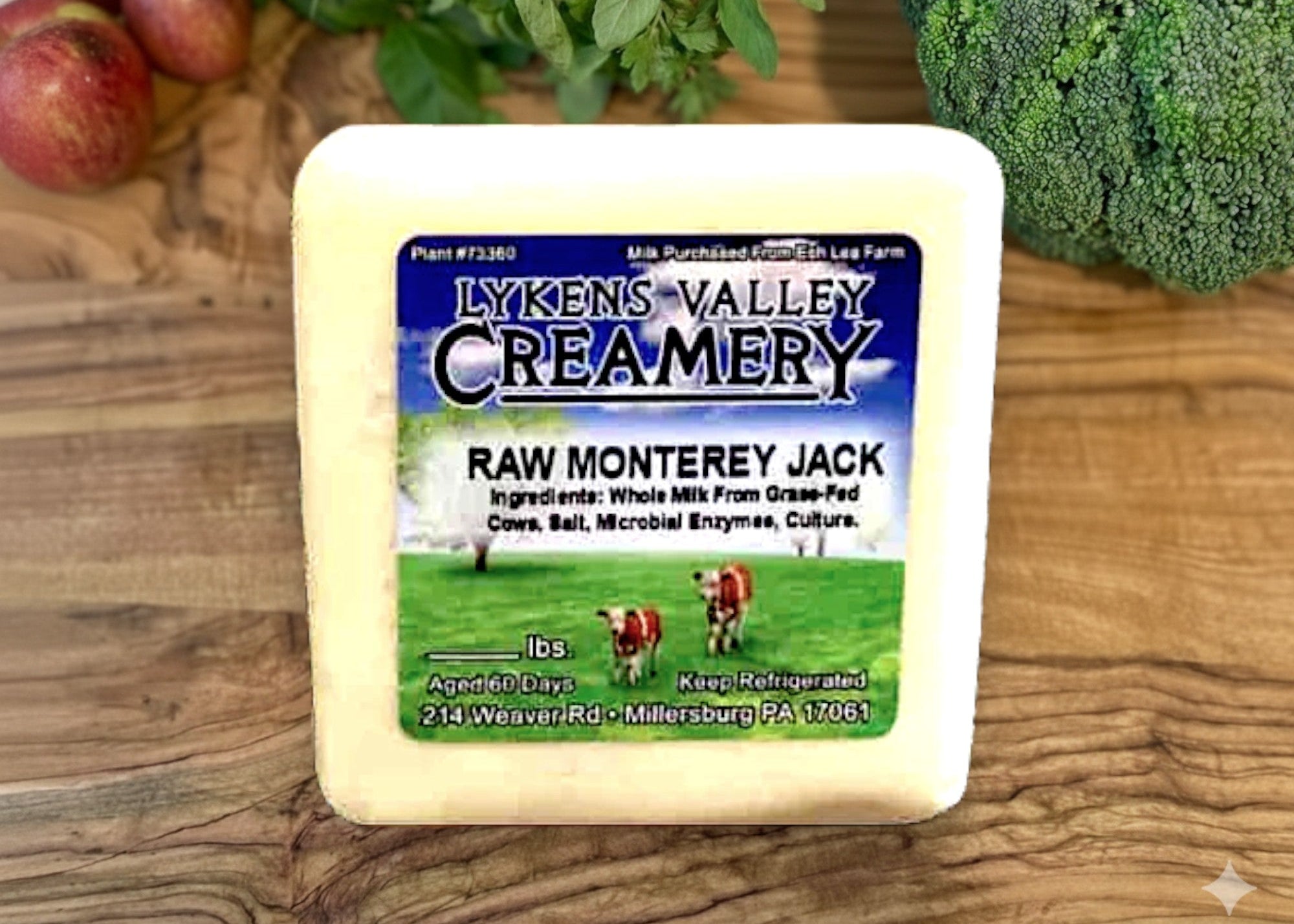 Block of Lyken's Valley Creamery Raw Monterey Jack cheese on a wooden surface with vegetables in the background.