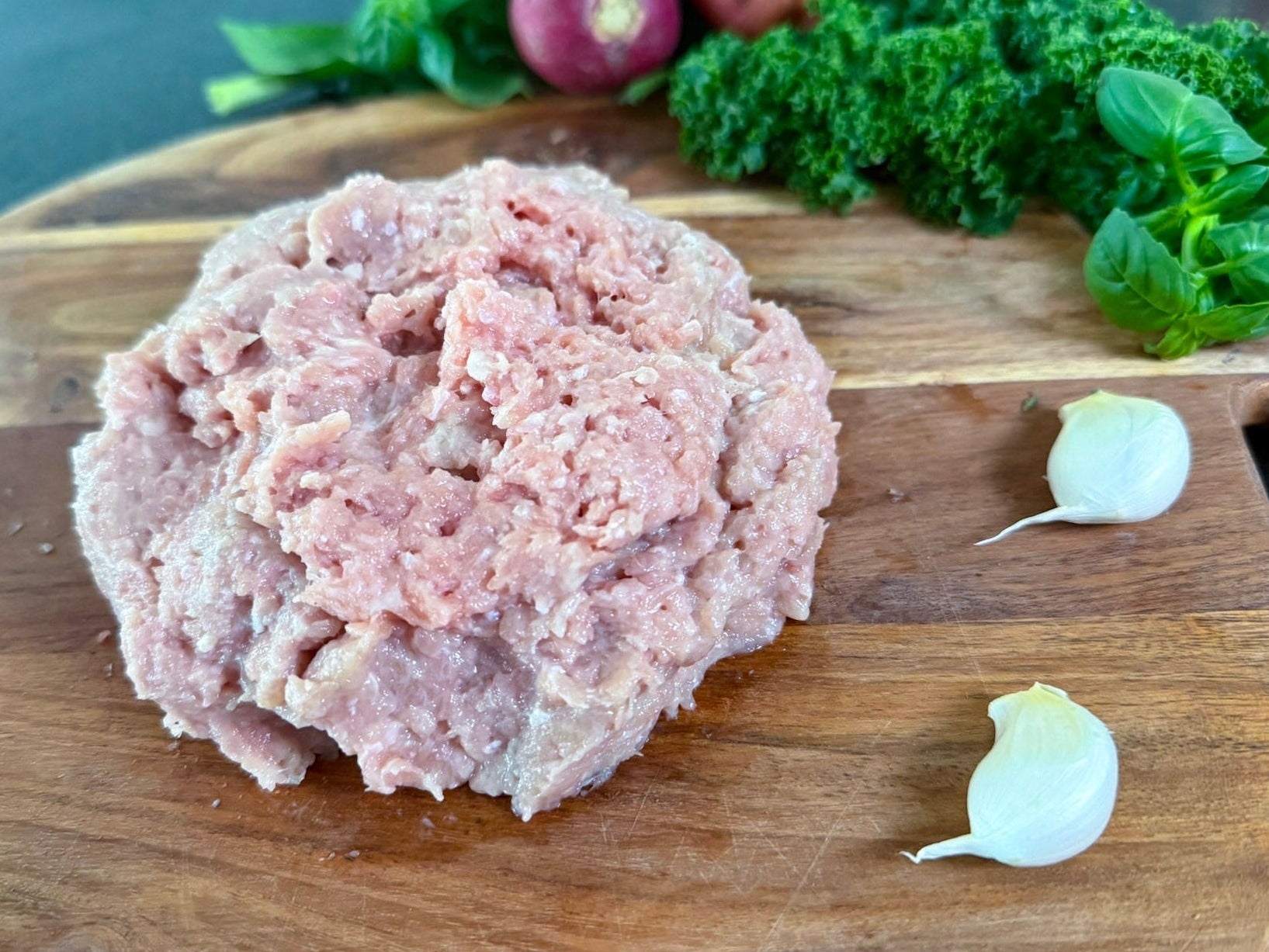 Raw pasture raised ground chicken on a wooden cutting board with vegetables in the background