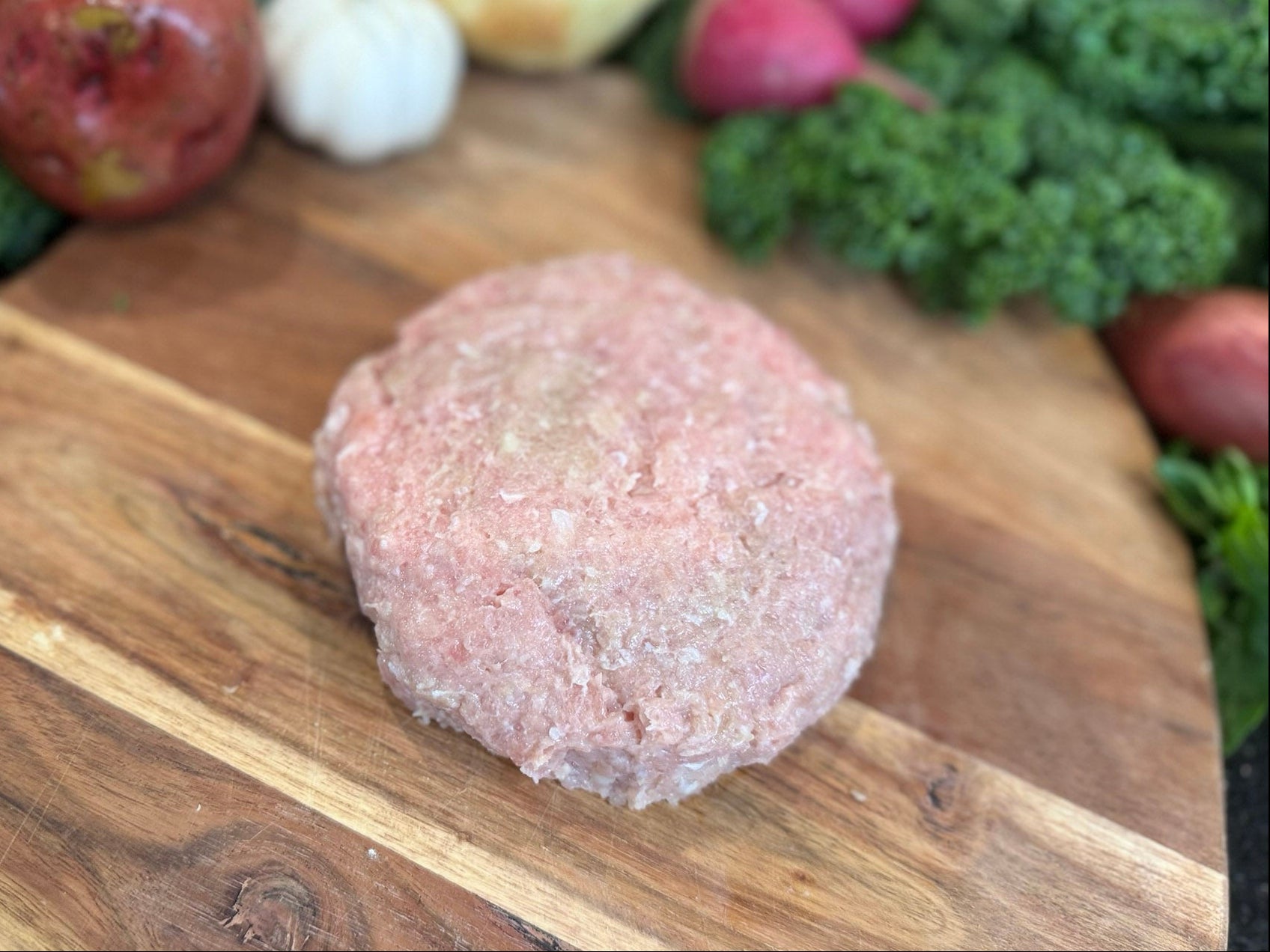 Raw ground pork on a wooden cutting board with vegetables in the background
