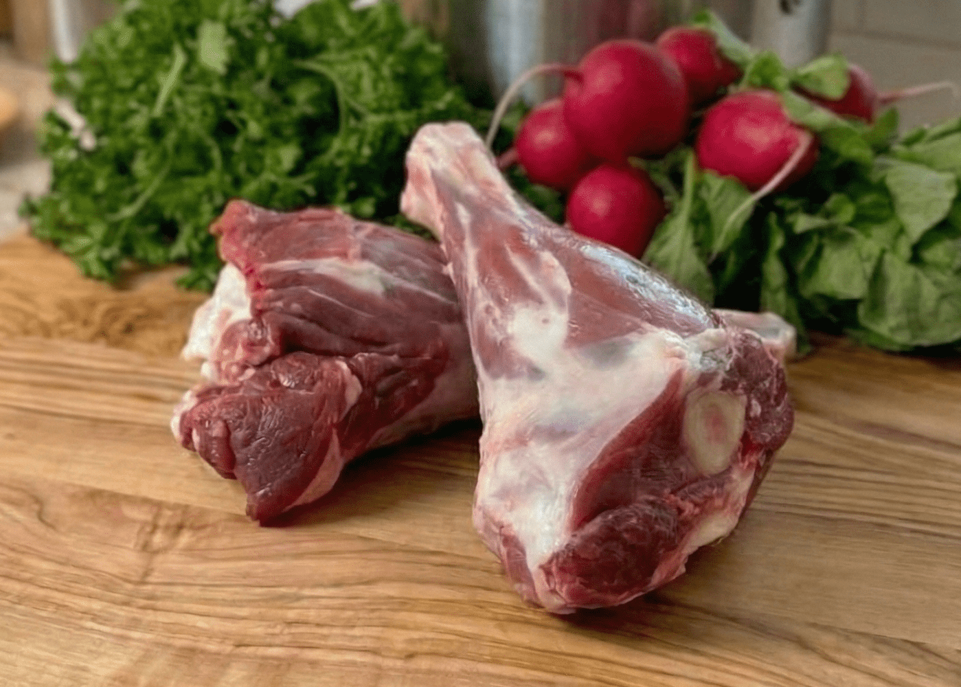 Raw pasture raised Lamb Shanks on a wooden cutting board with fresh vegetables in a kitchen setting