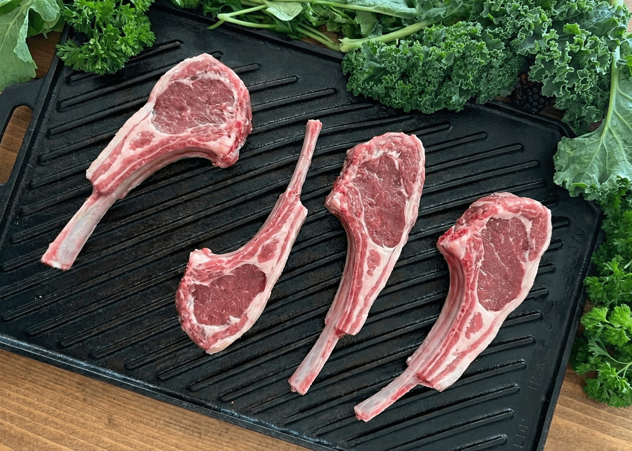 Raw pasture raised lamb rib chops on a grill pan with fresh vegetables on a wooden surface