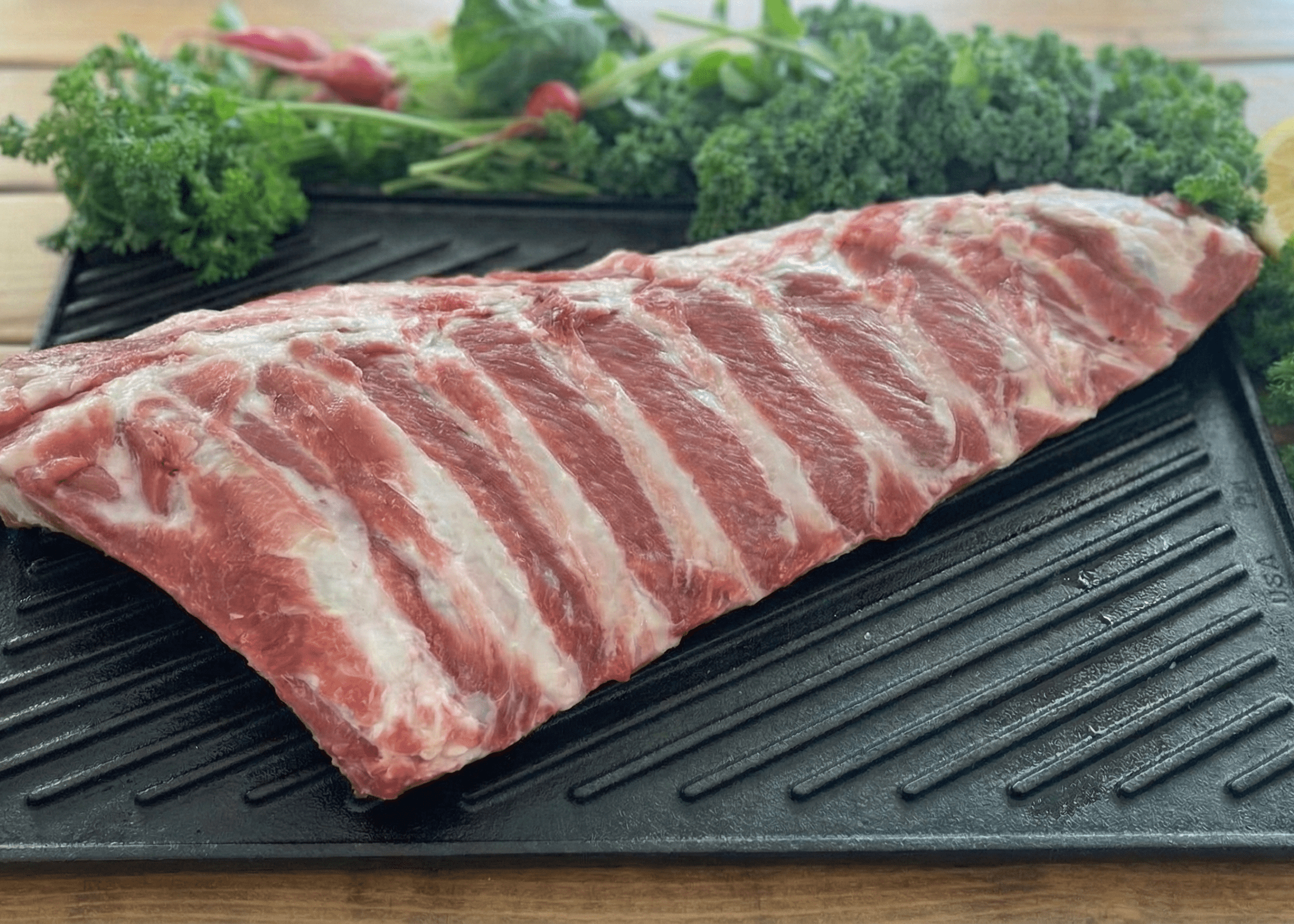 Raw pork ribs on a grill pan with vegetables on a wooden surface