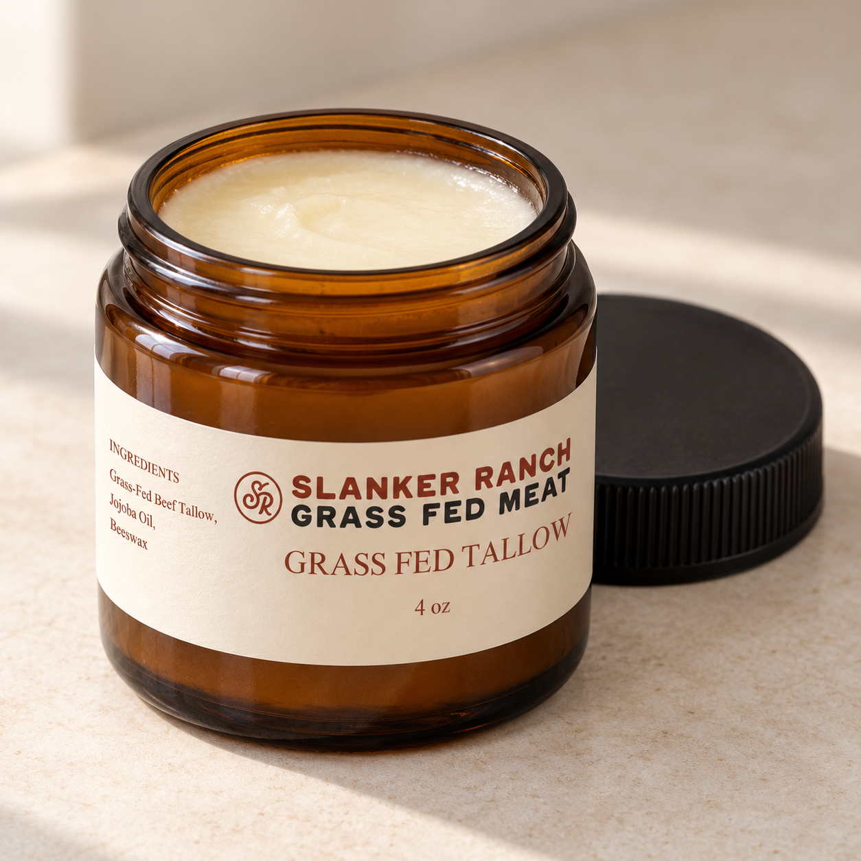 Open 4 oz amber glass jar filled with Slanker Ranch grass-fed tallow cream, with the black lid beside it.