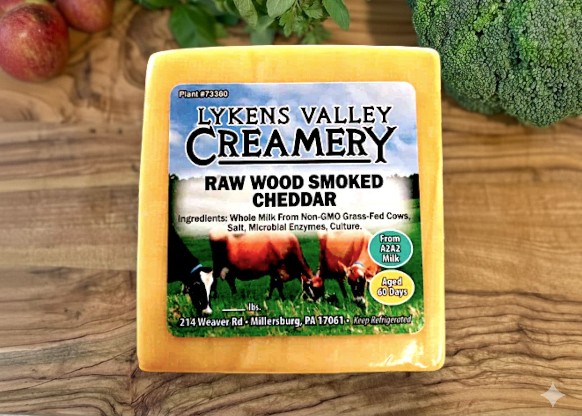 Lykens Valley Creamery raw wood smoked cheddar cheese on a wooden surface with fruits and vegetables.